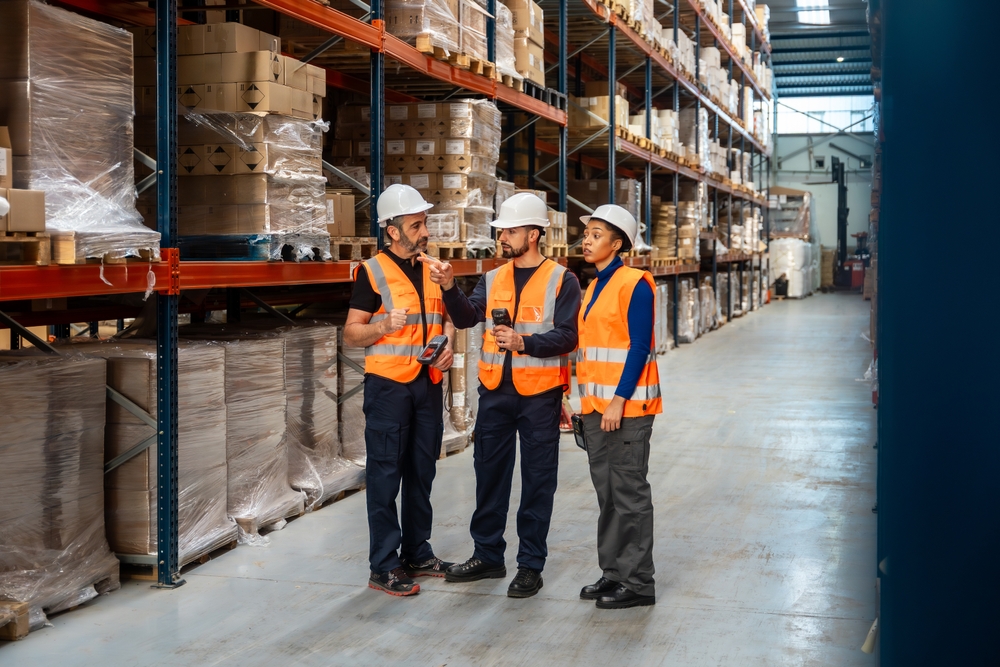 Industrial team meeting beside production equipment while planning Supply Chain Optimization for greater operational efficiency.