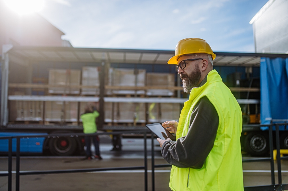 Warehouse operations manager reviewing dock and pallet flow data on a tablet during a logistics simulation planning session
