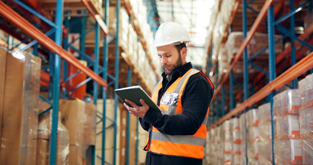 Operations manager checking warehouse optimization results on a tablet while standing on the warehouse floor
